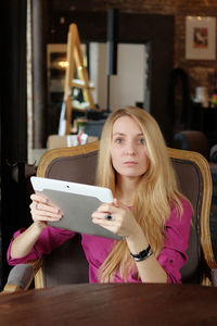 Portrait of young woman using phone while sitting on chair