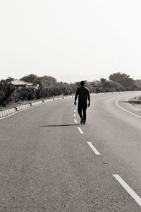 Rear view of man walking on road against clear sky