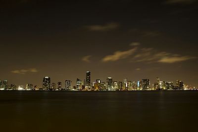 Illuminated cityscape at miami beach against sky at night