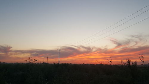 Silhouette electricity pylon on field against romantic sky at sunset