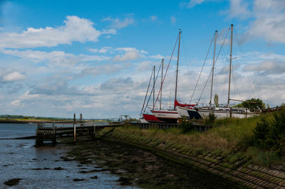 Sailboats moored on pier by sea against sky