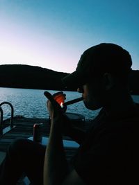 Side view of man holding cigarette in sea against clear sky