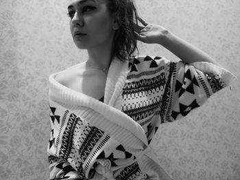 Woman wearing bathrobe with hand in hair looking away while standing against wall