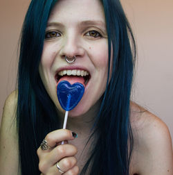 Portrait of smiling young woman licking heart shape candy