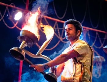 Side view of man holding burning fire at night