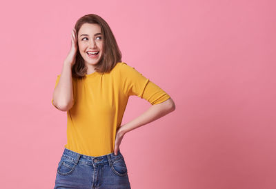 Portrait of smiling young woman standing against pink background