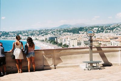 Rear view of woman standing against sea and cityscape