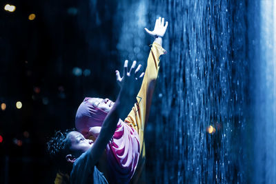 Teenage girl with brother standing by artificial waterfall at night