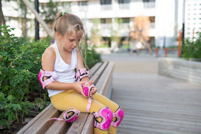 Girl putting on protective pads sitting on bench
