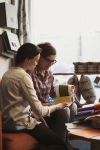 Smiling owner showing fabric swatches to customer while sitting at store