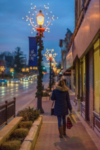 Woman walking on illuminated sidewalk at night