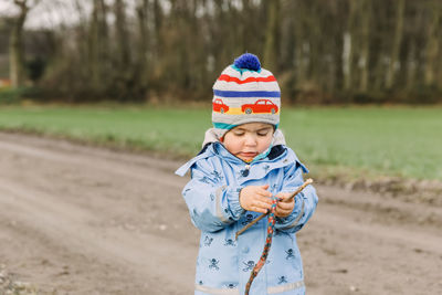 Cute girl holding stick while standing on land in forest