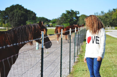 Woman standing by horses in fence on field