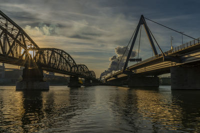 Silhouette bridge over river against sky during sunset