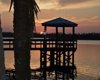 Silhouette gazebo by sea against sky during sunset