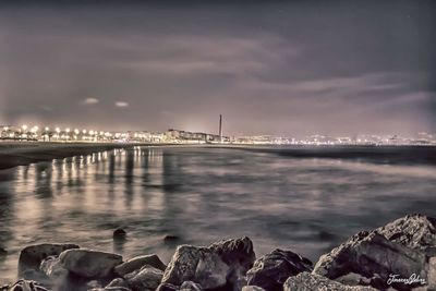 View of river in front of illuminated bridge at night