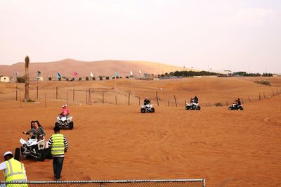 People riding quadbikes at desert against sky