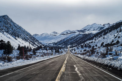 Road leading towards snowcapped mountains against sky