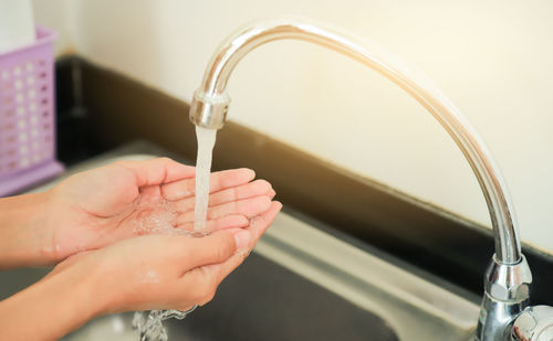 Cropped image of hand holding faucet against water
