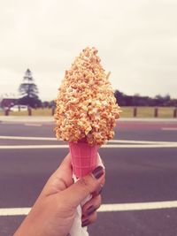 Hand holding ice cream cone against sky