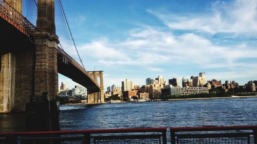 Bridge over river by buildings in city against sky