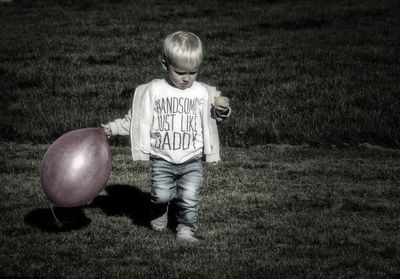 Full length of boy holding balloon while walking on grassy field at park