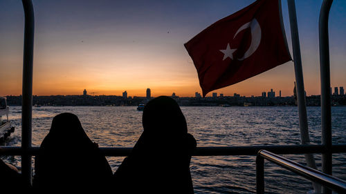 Rear view of woman sitting on beach against sky during sunset
