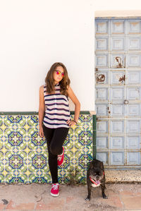 Girl standing with dog against wall