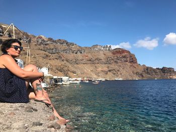 Young woman on rock by sea against sky