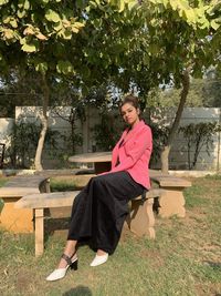 Young woman sitting on seat against trees