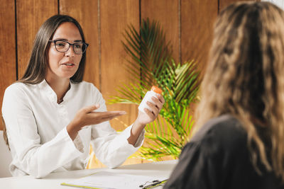 Portrait of young woman holding eyeglasses on table