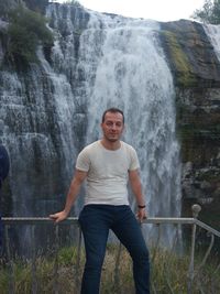 Portrait of man sitting on railing against waterfall