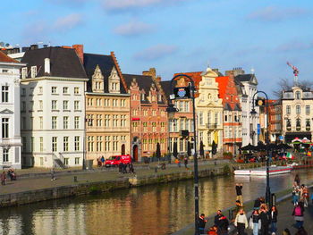 People on river by buildings in city against sky