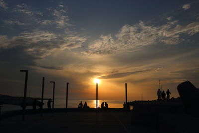 Silhouette people by sea against sky during sunset