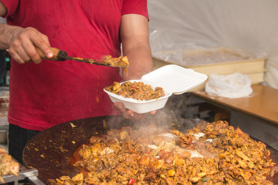 Midsection of vendor holding meat in container at stall