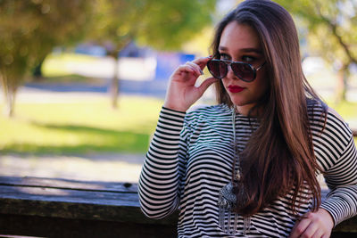 Young woman wearing sunglasses while standing against wood at park
