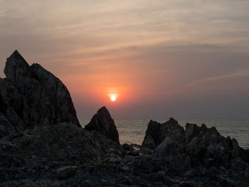 Rock formations by sea against sky during sunset