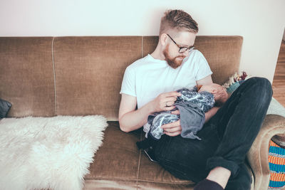 Mid adult man looking at baby boy while sitting on sofa