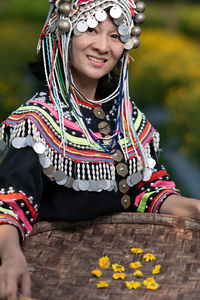 Portrait of smiling woman in traditional clothing holding straw basket standing at farm