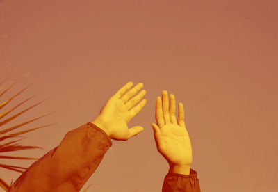 Close-up of hands against orange sky