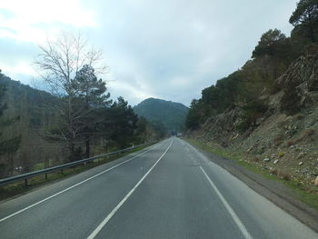 Empty road along trees and mountains against sky