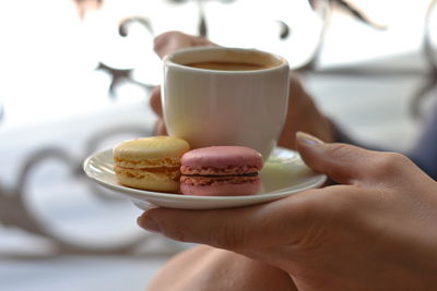 Cropped image of woman holding coffee cup with macaroons in saucer