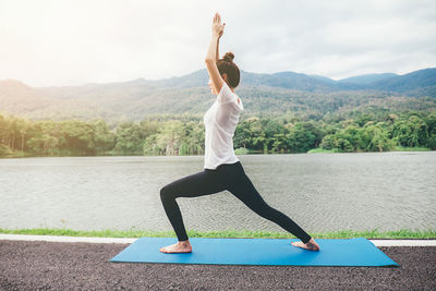 Woman doing yoga at lakeshore against sky