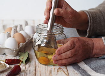 .an elderly woman prepares homemade mayonnaise in a jar with vegetable oil and an egg.