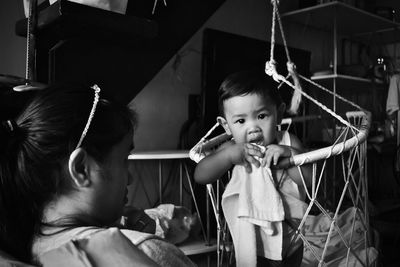 Portrait of boy standing in crib by mother at home