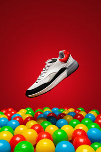 Shoe levitating over multi colored balls against red background