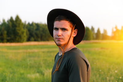 Young man farmer in cowboy hat at agricultural field on sunset with sun flare. portrait 