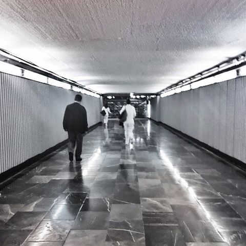 indoors, walking, full length, ceiling, lifestyles, men, tunnel, architecture, the way forward, rear view, built structure, illuminated, corridor, wall - building feature, leisure activity, lighting equipment, person, diminishing perspective