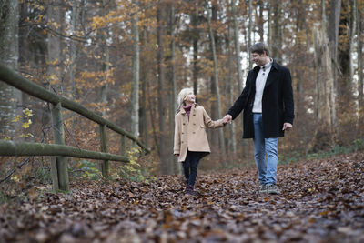 Happy girl holding hand of father and walking in autumn forest
