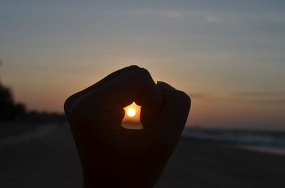 Close-up of hand holding sun during sunset